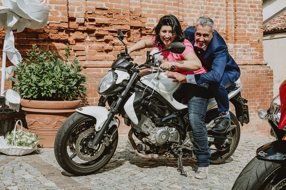 Fotografo Matrimonio in Piemonte. Cerimonia a Moriondo Torinese. Sposo davanti alla chiesasu di una motocicletta con un'amica.