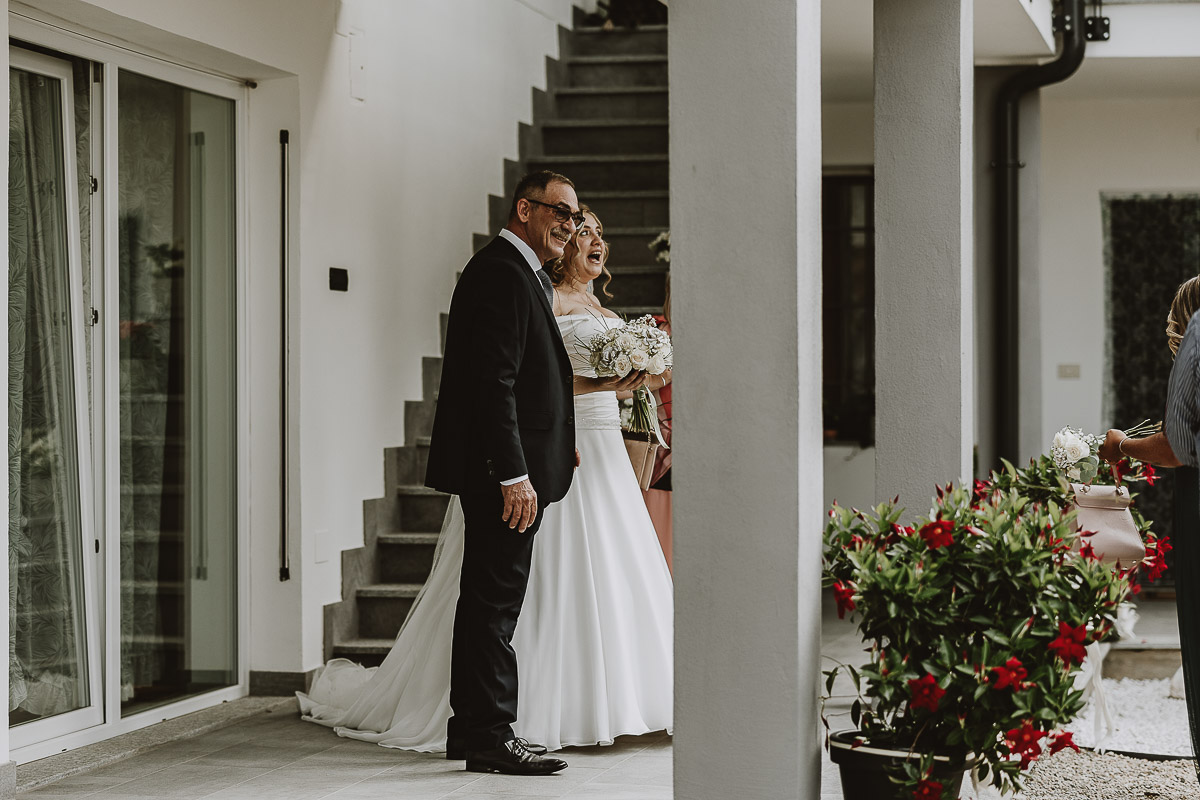 Fotografo Matrimonio in Piemonte. Preparazione a Moncucco Torinese. Sposa con il padre sotto il portico.
