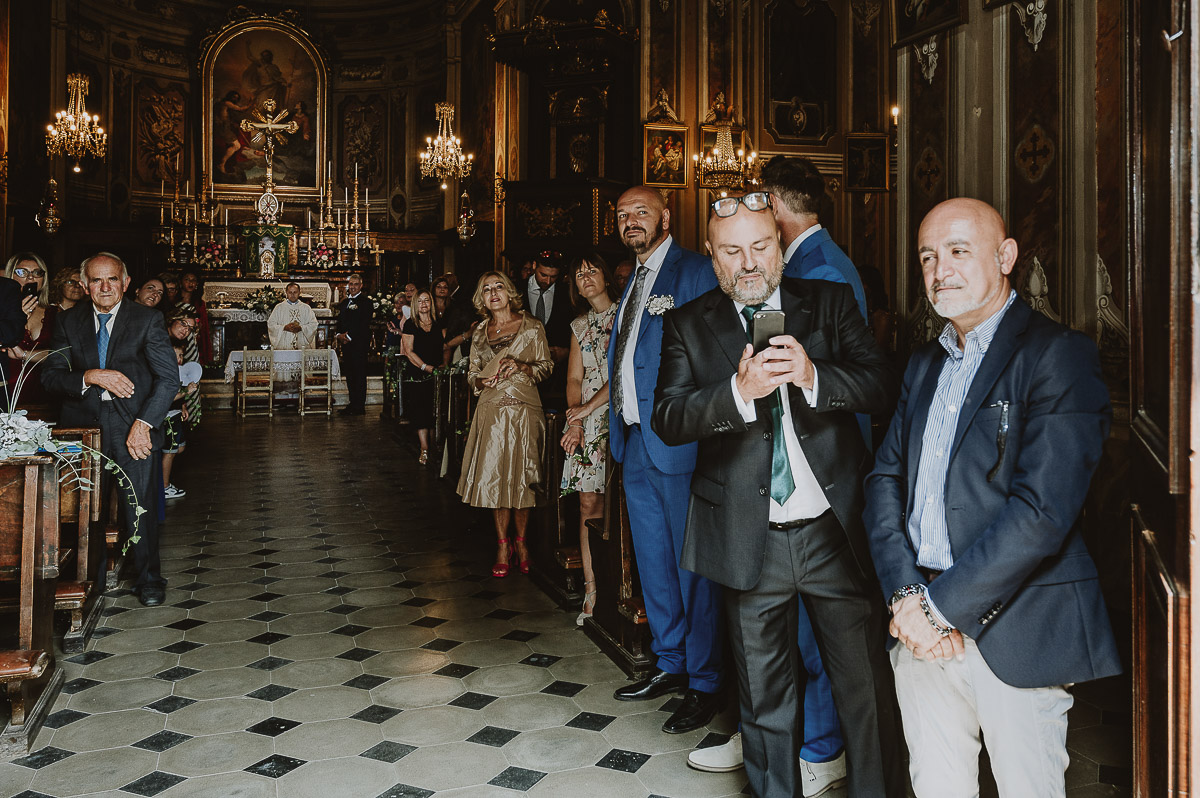 Fotografo Matrimonio in Piemonte. Cerimonia nella chiesa di San Giovanni Battista di Moriondo Torinese. Gli invitati guardano fuori perchè aspettano l'arrivo della sposa