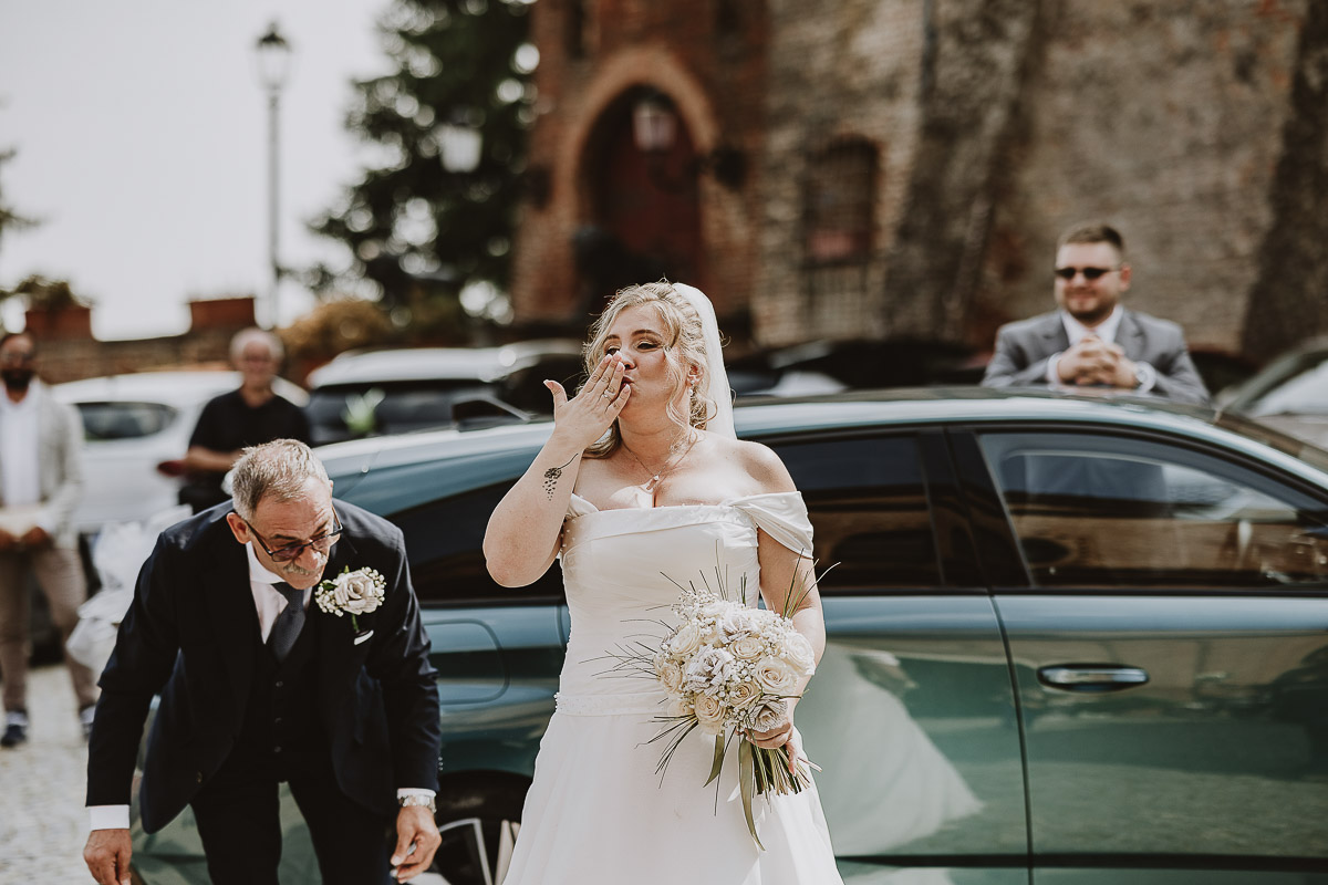 Fotografo Matrimonio in Piemonte. Cerimonia nella chiesa di San Giovanni Battista di Moriondo Torinese. Arrivo della sposa che manda baci a tutti.