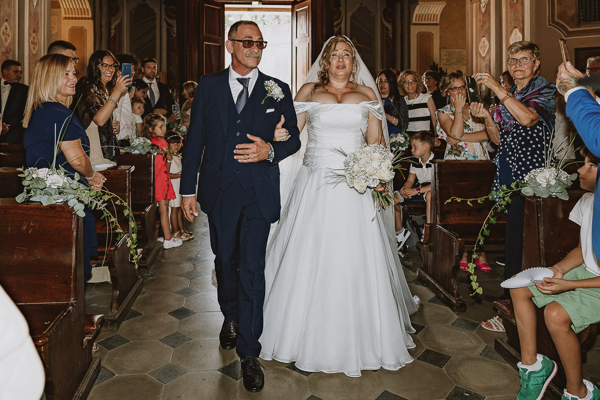 Fotografo Matrimonio in Piemonte. Cerimonia nella chiesa di San Giovanni Battista di Moriondo Torinese. Entrata in chiesa della sposa con il padre.