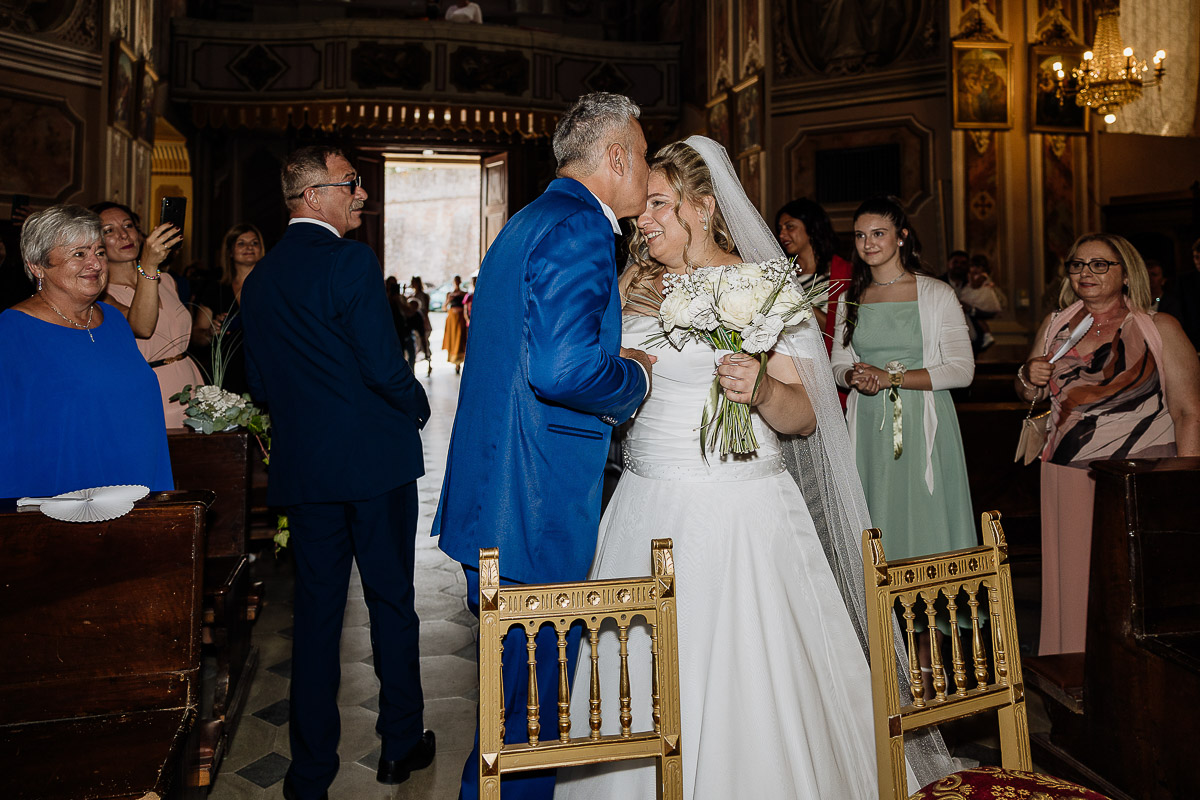 Fotografo Matrimonio in Piemonte. Cerimonia nella chiesa di San Giovanni Battista di Moriondo Torinese. Sposo bacia la sposa sulla fronte.