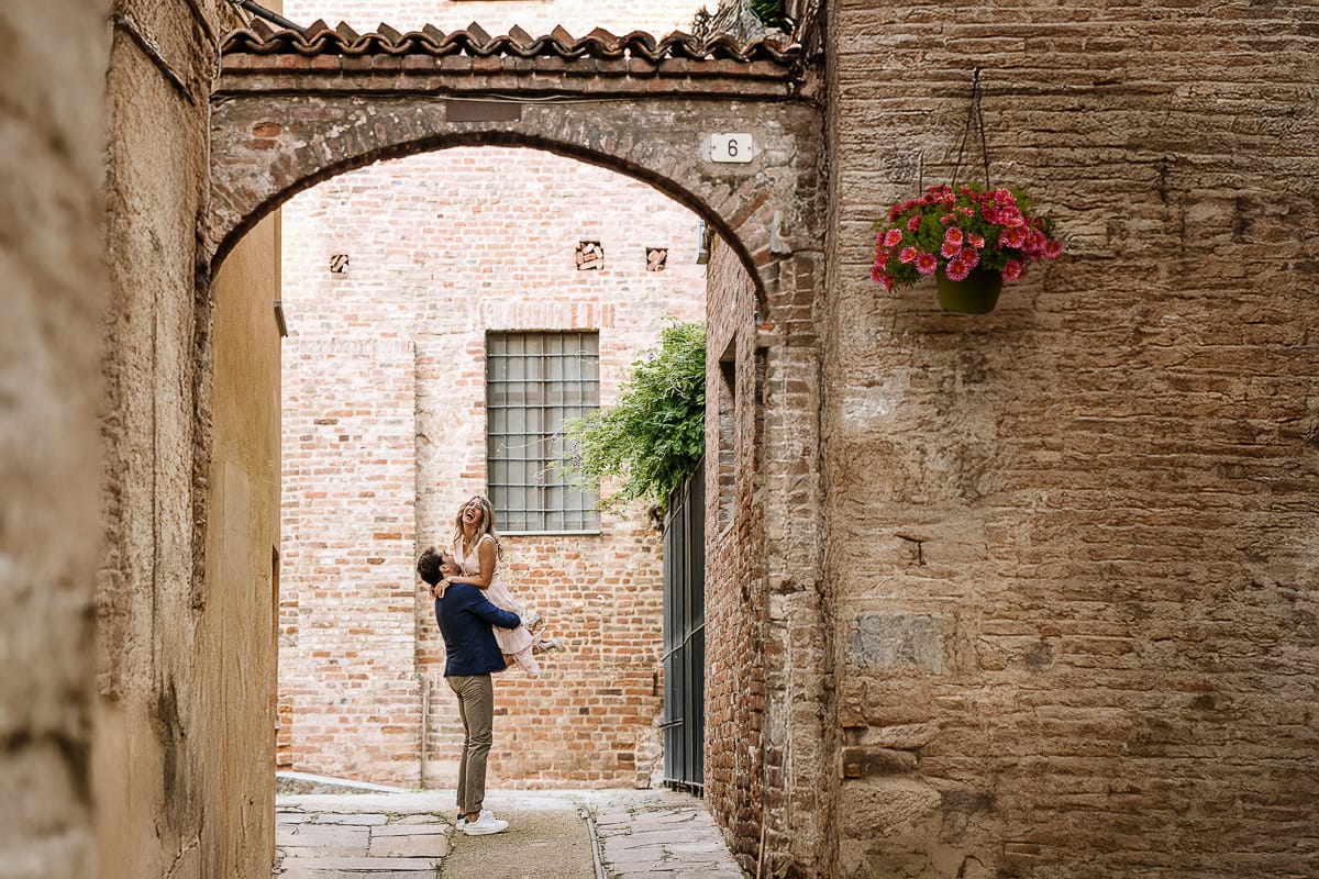 Pre-wedding a Chieri. Claudio prende in braccio Shary sooto un arco di un palazzo medievale.