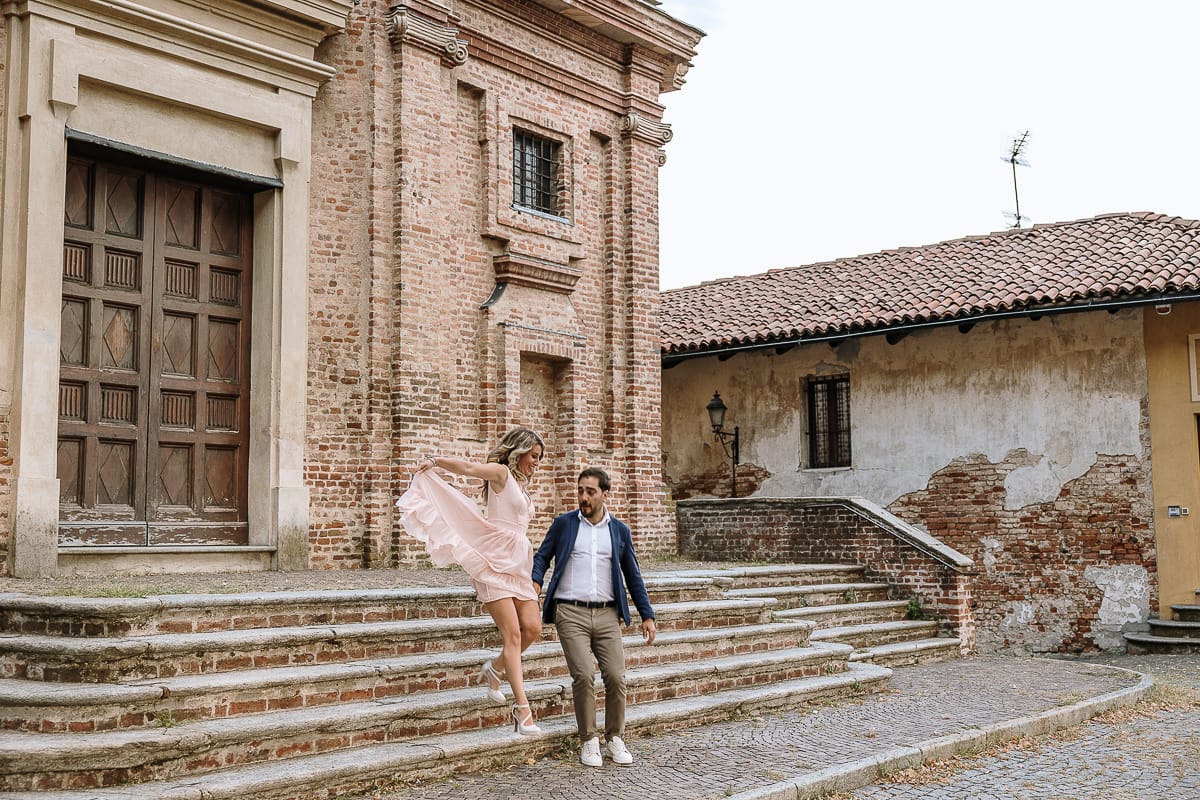 Pre-wedding a Chieri. Shary e Claudio nel piazzale della Chiesa di San Giorgio, il punto più alto e panoramico della città. Shary e Claudio davanti al portone della chiesa scendono le scale. Saltano lì'ultimo gradino.