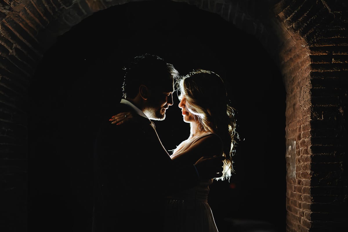 Pre-wedding a Chieri. Shary e Claudio abbracciati davanti all'ingresso delle ex-carceri medievali. Flash off-camera dietro di loro che crea rim light.