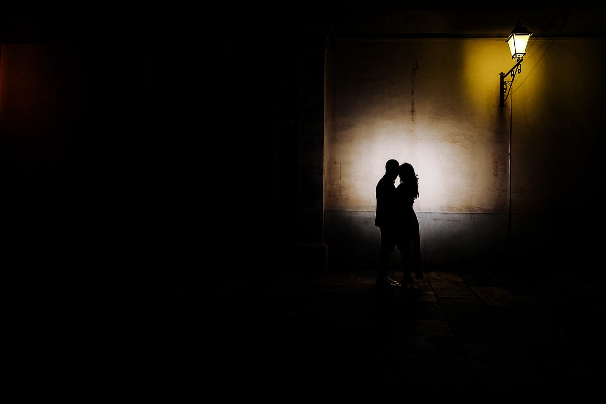 Pre-wedding a Chieri. Shary e Claudio davanti ad un portone, vicino ad un lampione acceso.. Foto serale. Flash dietro di loro puntato sul muro. Silhouette.