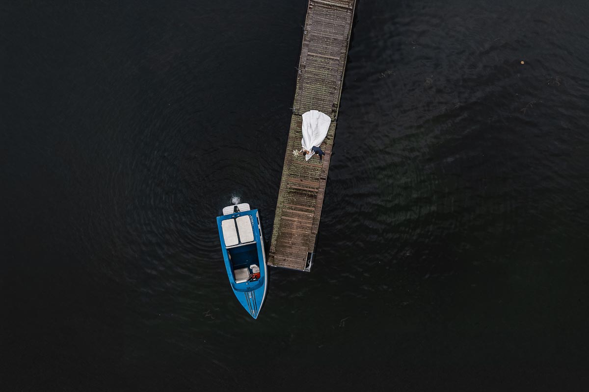 Fotografo Matrimonio Lago di Viverone, Tenuta Variselle. Ritratti di coppia. Sposi sul pontile sul lago. Foto dal drone Sposi camminano sul pontile sul lago verso il motoscafo azzurro.