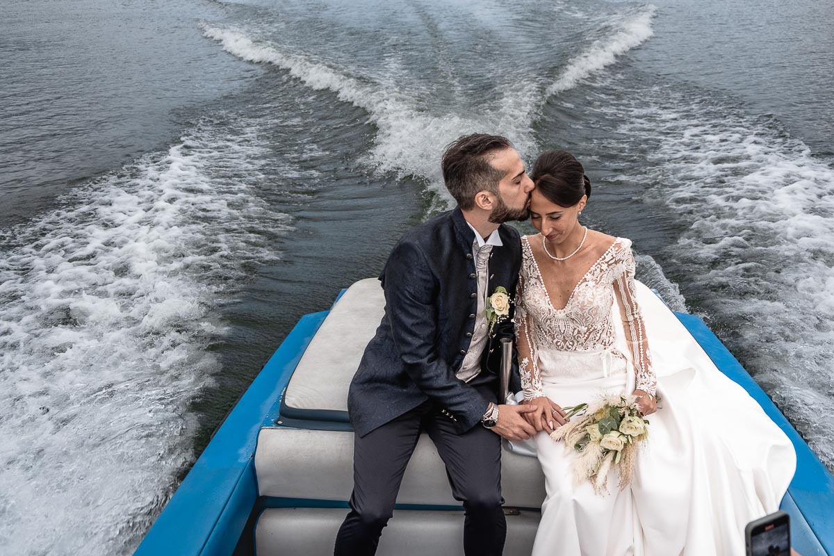 Fotografo Matrimonio Lago di Viverone, Tenuta Variselle. Fotografia di coppia degli sposi. Sposi sul motoscafo. Sposo bacia sposa sulla tempia.