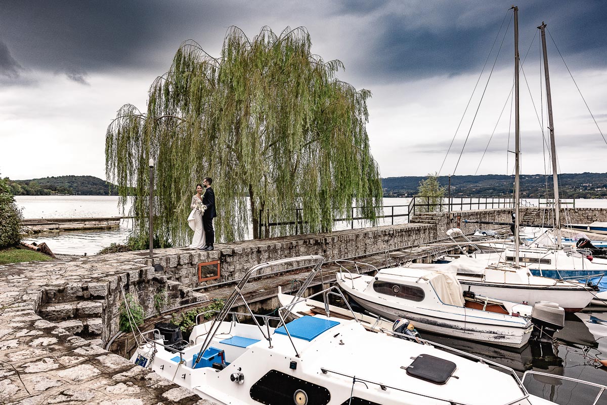 Fotografo Matrimonio Lago di Viverone, Tenuta Variselle. Fotografia di coppia degli sposi. Sposi sul pontile. Sposi sotto il salice, di fronte al porticciolo turistico.