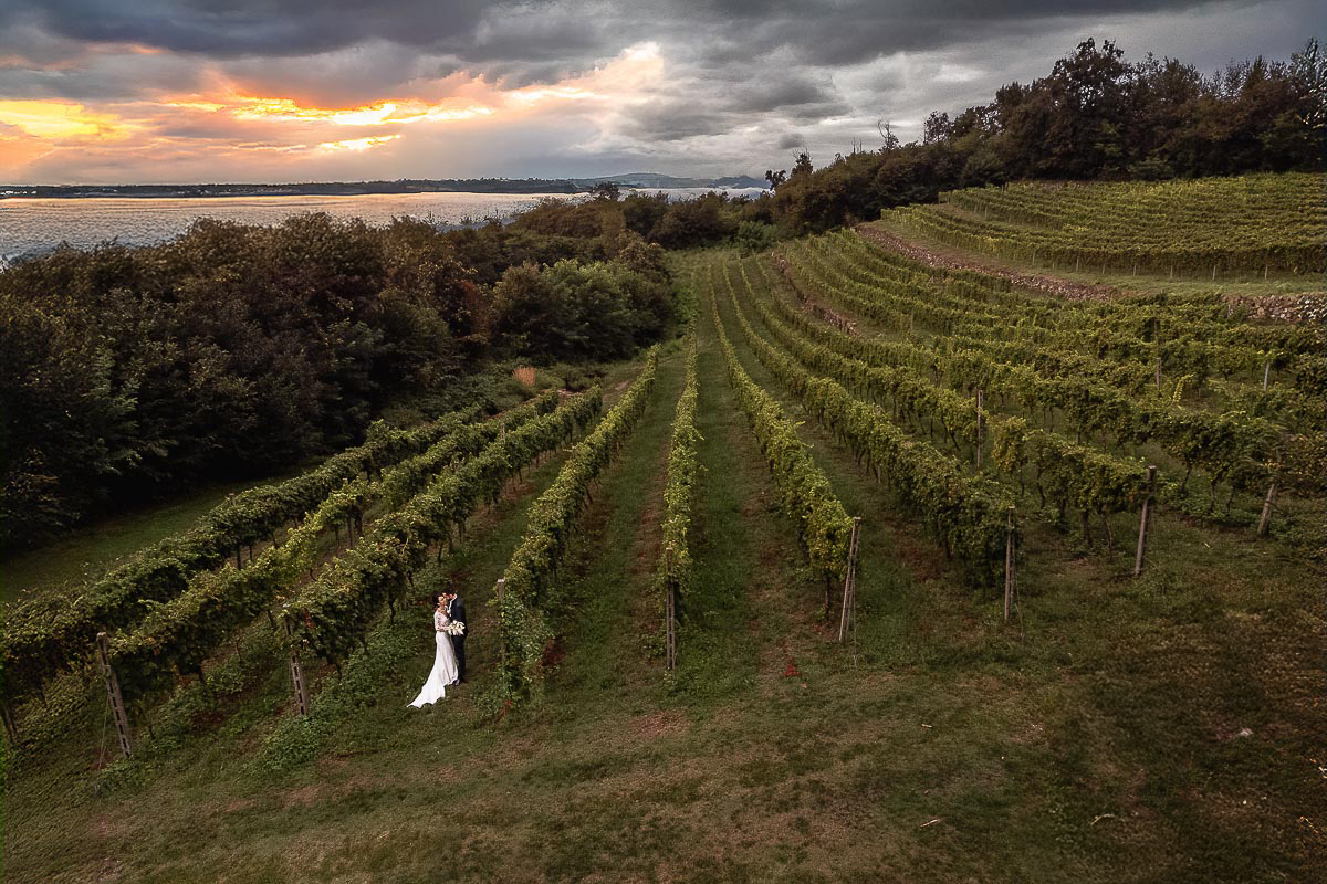 Fotografo Matrimonio Lago di Viverone, Tenuta Variselle. Sessione di coppia preserale nel vigneto. Panoramica con vista lago in lontannaza e squarcio di sole che tramonta.