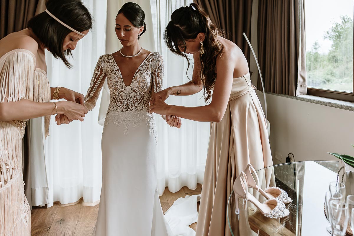 Fotografo Matrimonio Lago di Viverone, Tenuta Variselle. Preparazione della sposa. Sorelle aiutano la sposa a vestirsi.