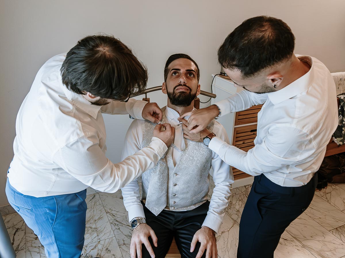 Fotografo Matrimonio Lago di Viverone, Tenuta Variselle. Preparazione dello sposo. Testimoni aiutano lo sposo a vestirsi.