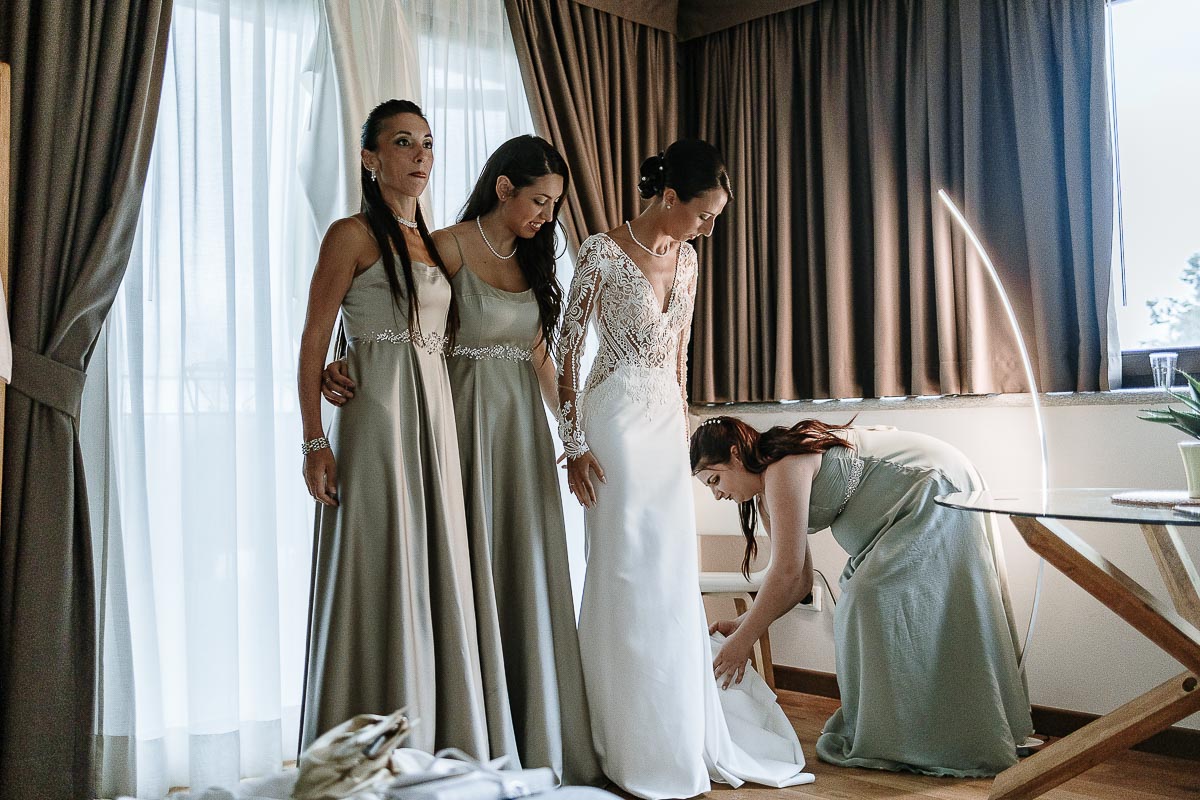 Fotografo Matrimonio Lago di Viverone, Tenuta Variselle. Preparazione della sposa. sposa con le damigelle. Una damigella le sistema il vestito.