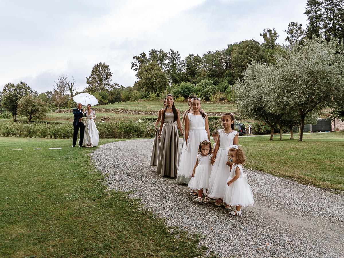 Fotografo Matrimonio Lago di Viverone, Tenuta Variselle. Cerimonia religiosa secondo il rito della Chiesa di Antiochia. Corteo delle damigelle, mentre la sposa con il padre attendono sotto lìombrello perchè è iniziato a piovere.