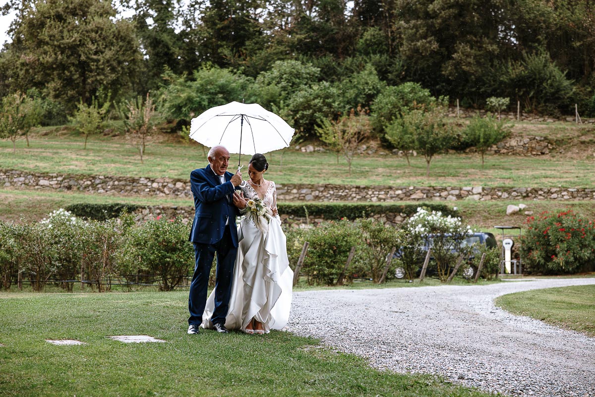 Fotografo Matrimonio Lago di Viverone, Tenuta Variselle. Cerimonia religiosa secondo il rito della Chiesa di Antiochia. sposa con il padre sotto l'ombrello.