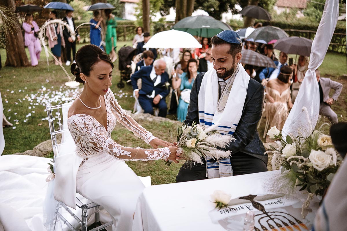 Fotografo Matrimonio Lago di Viverone, Tenuta Variselle. Cerimonia religiosa secondo il rito della Chiesa di Antiochia. Sposi seduti si danno la mano.