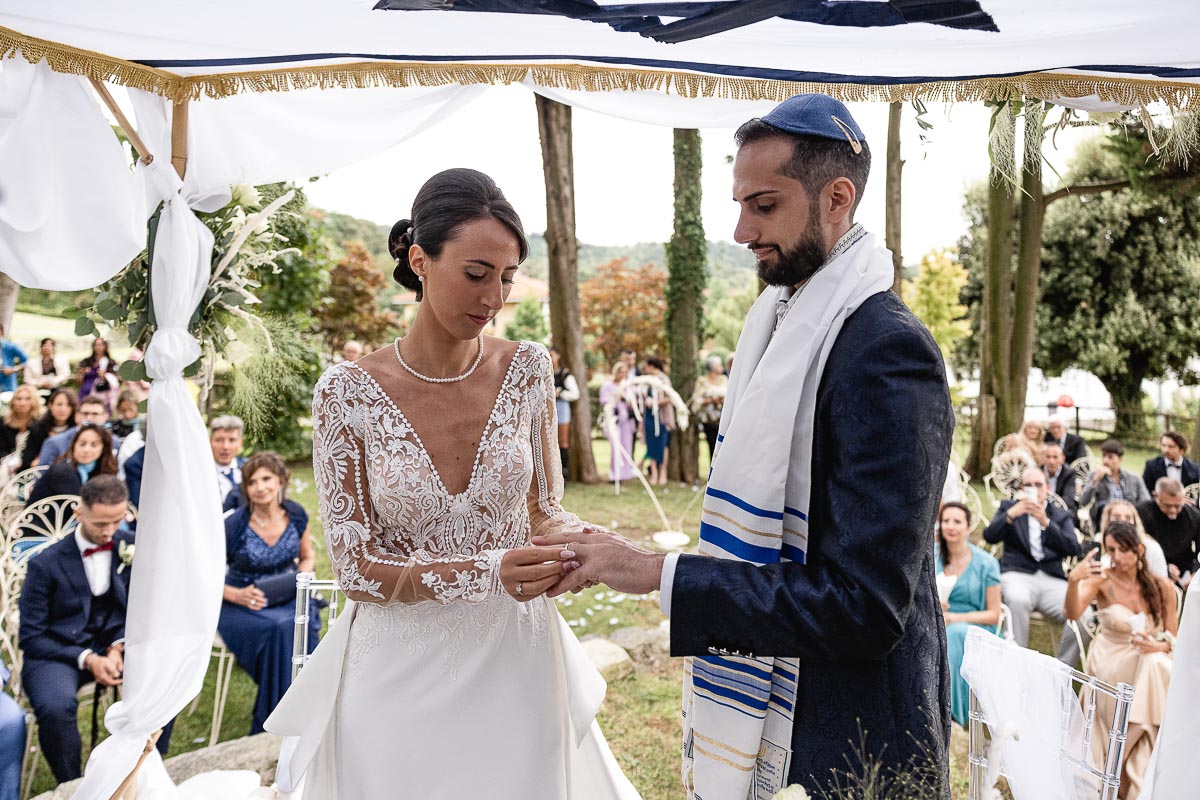 Fotografo Matrimonio Lago di Viverone, Tenuta Variselle. Cerimonia religiosa secondo il rito della Chiesa di Antiochia. Sposa mette l'anello al dito dello sposo.