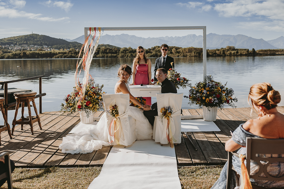 Matrimonio Lago di Candia. Cerimonia. Rito del calore. Sposi guardano gli invitati.