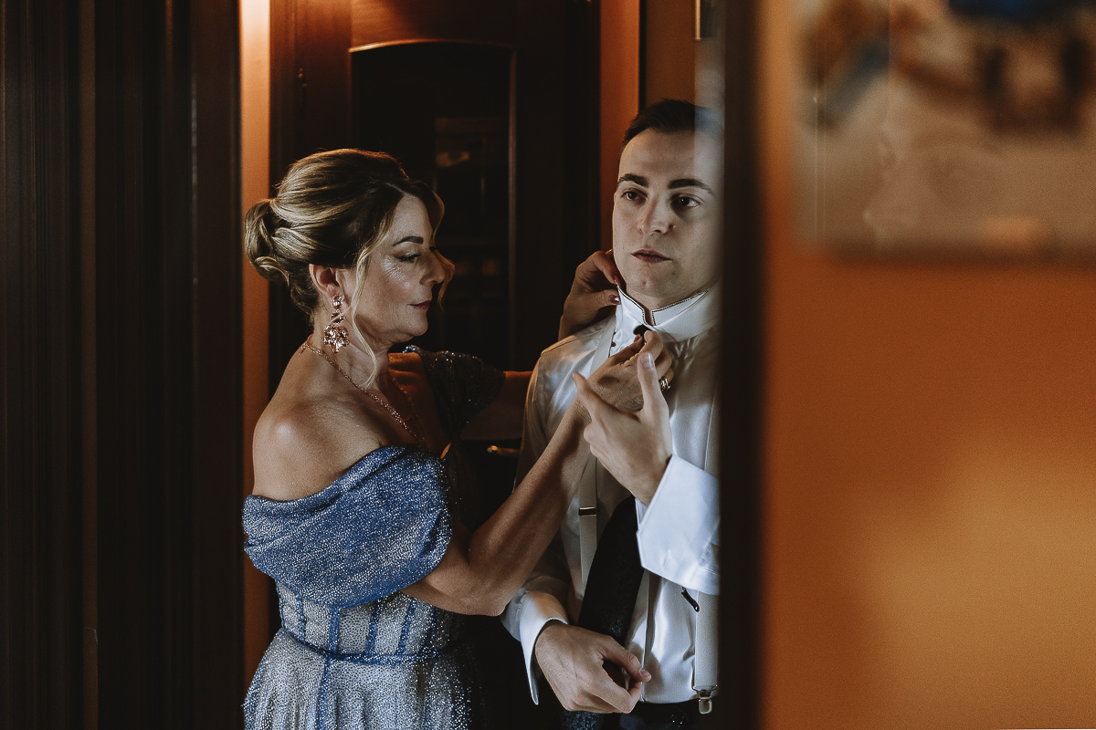 Matrimonio Lago di Candia . Preparazione dello sposo. Sposo e mamma riflessi allo specchio.