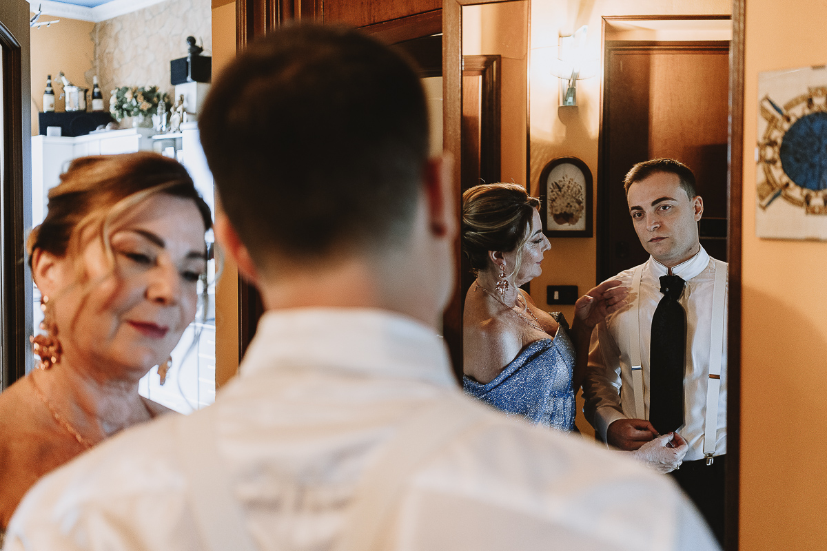 Matrimonio Lago di Candia . Preparazione dello sposo. mamma aiuta lo sposo a vestirsi, riflessi allo specchio.