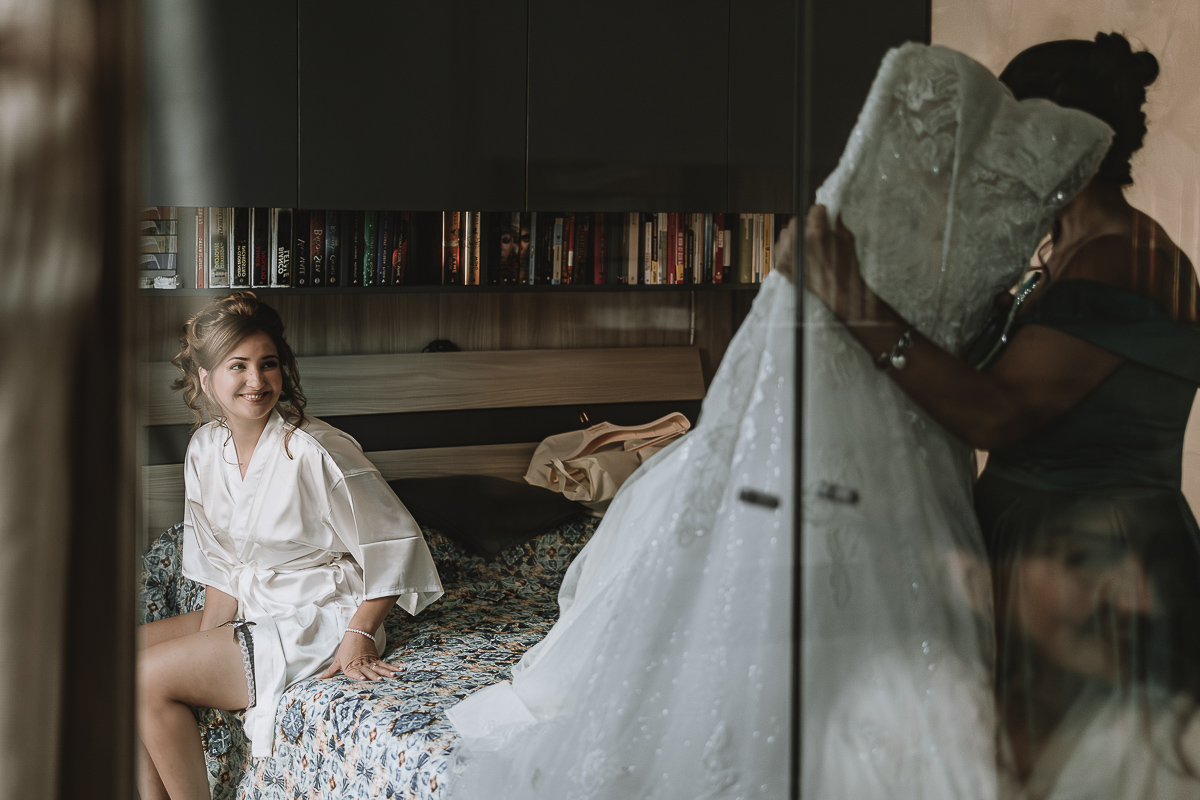 Matrimonio Lago di Candia . Preparazione della sposa. Sposa riflessa nello specchio dell'armadio guarda la mamma che tiene il suo abito da sposa.