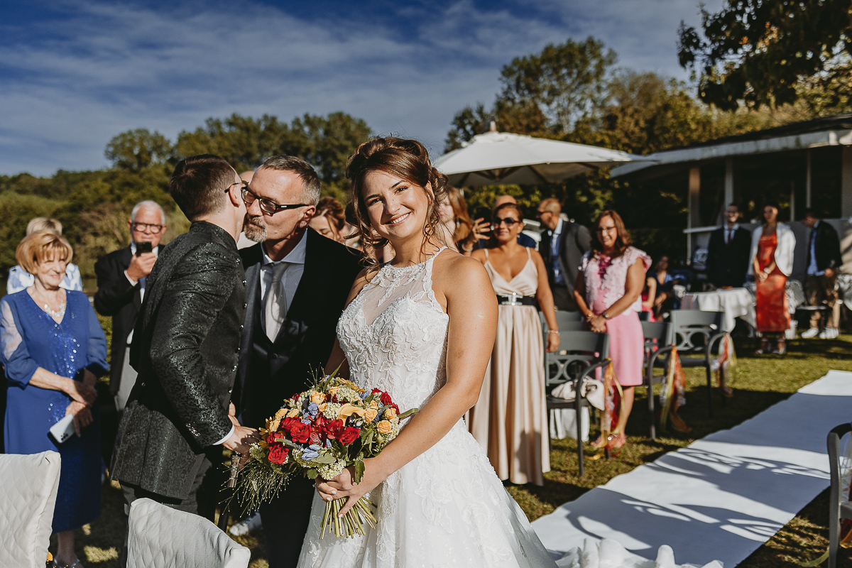 Matrimonio Lago di Candia. Cerimonia. Sposa fa l'ingresso nel luogo della cerimonia sul molo mentre lo sposo aspetta. Il padre bacia lo sposo.