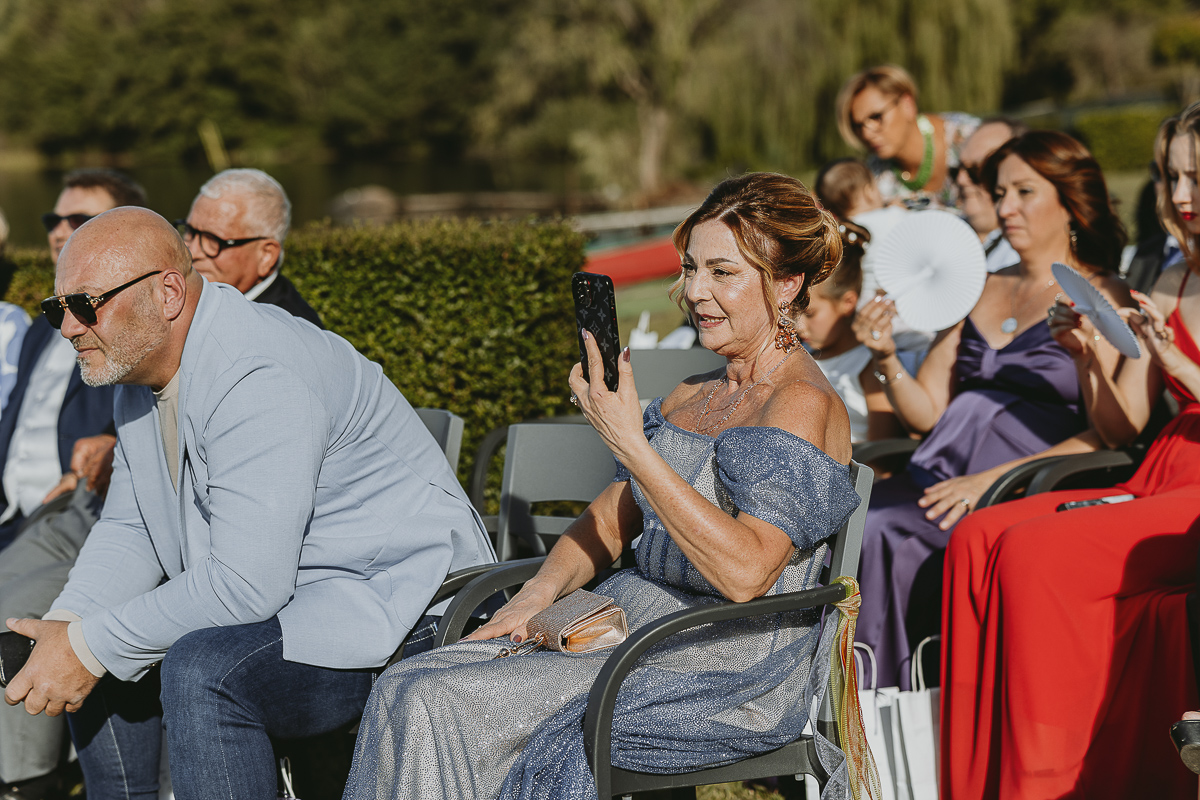 Matrimonio Lago di Candia. Cerimonia. Mamma dello sposo filma la cerimonia con il telefono.