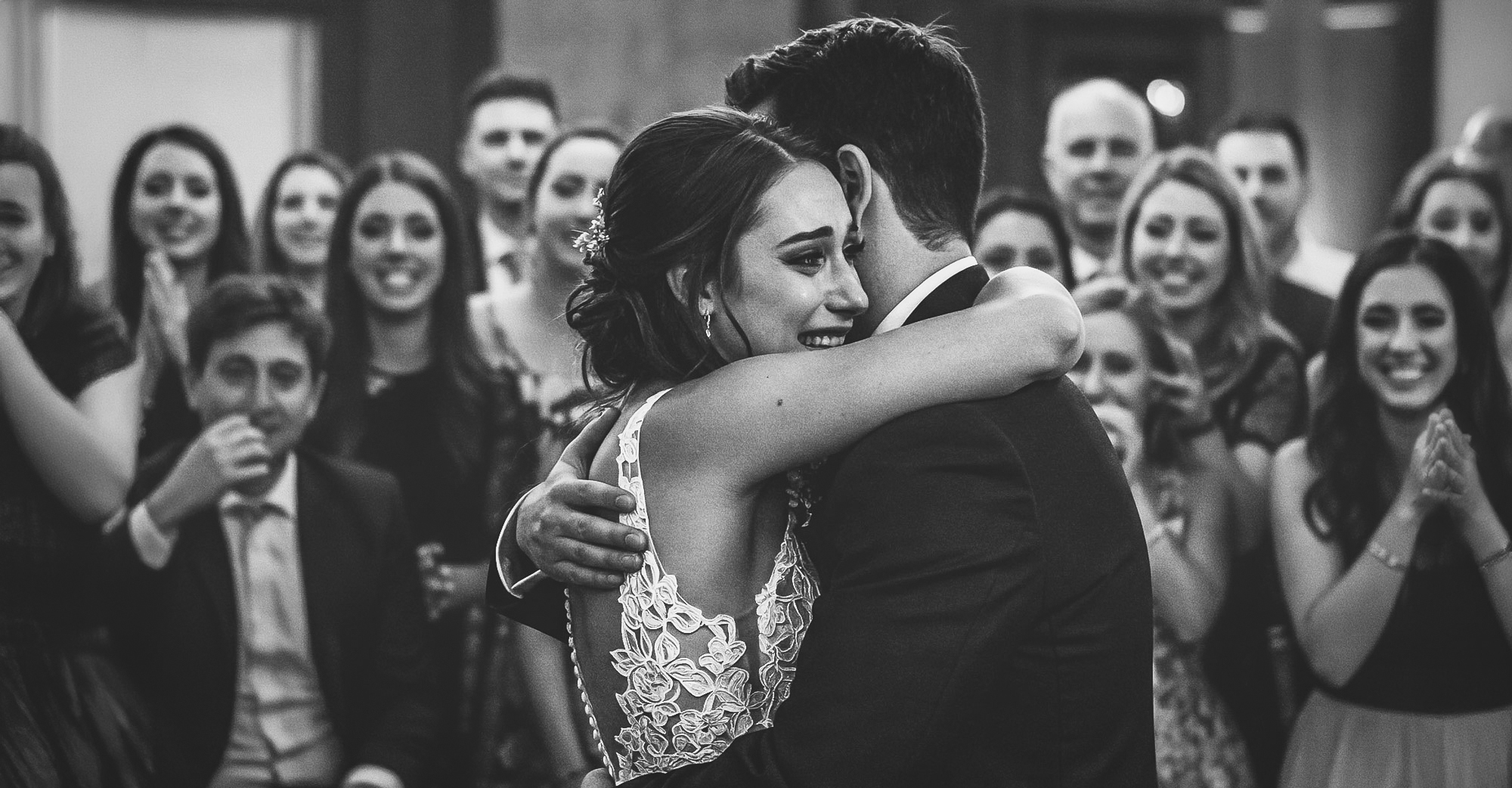 Fotografo di matrimonio – sposi emozionati si abbracciano durante il primo ballo, circondati dagli invitati commossi