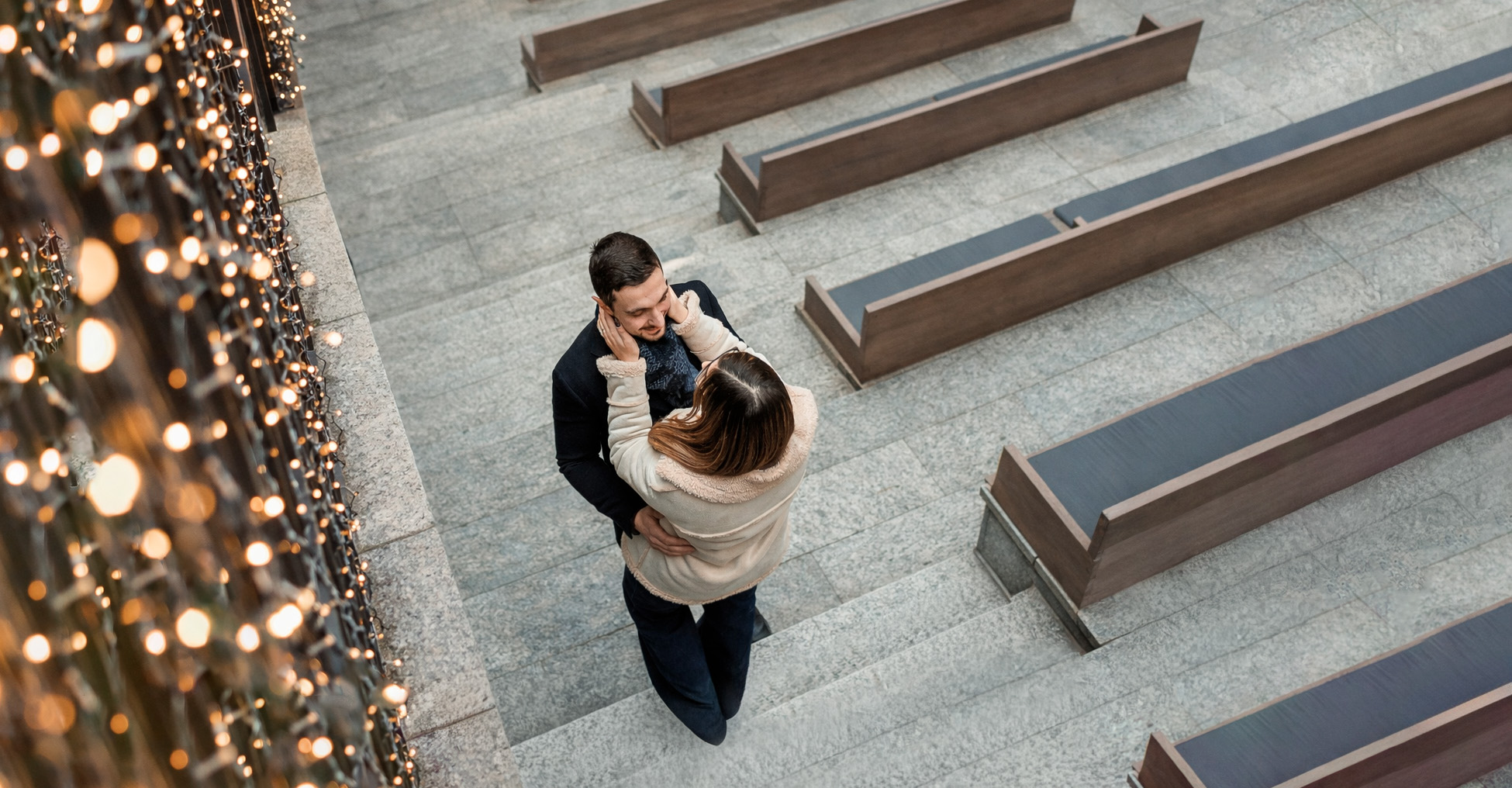 Prewedding natalizio a Torino di Beatrice e Gianluca, coppia abbracciata vista dall’alto nel bosco urbano delle Gallerie d’Italia, tra luci di Natale e geometrie architettoniche